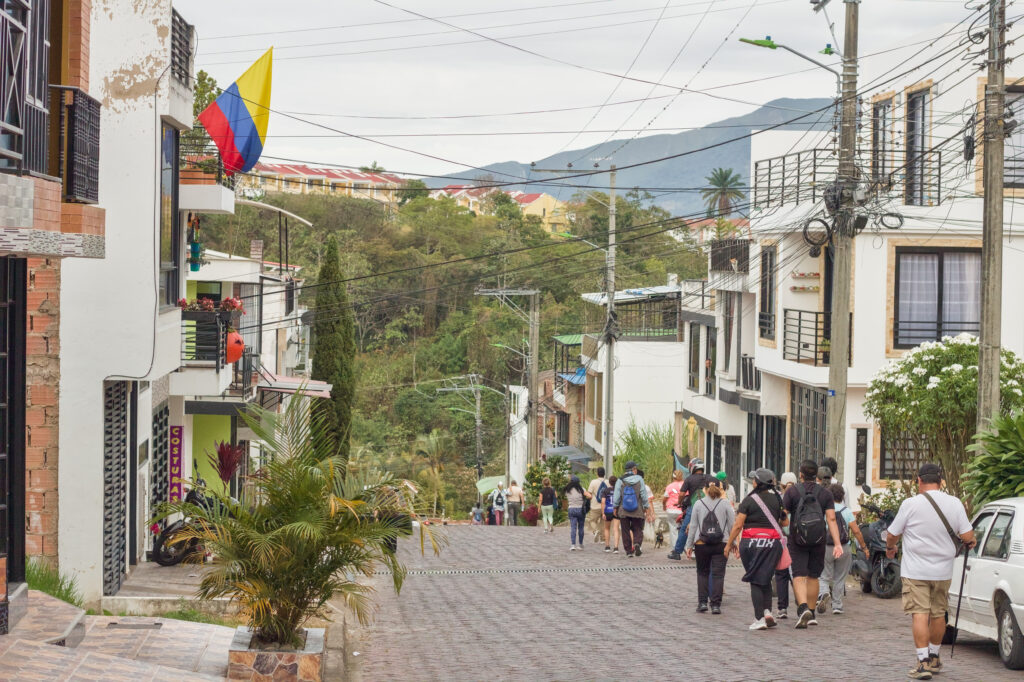 Caminata Tres Esquinas en Fusagasugá: Crónica, Ruta y Fotos (2026) 30 Senderistas caminando por calle adoquinada de Villa Natalia con bandera colombiana en Fusagasuga